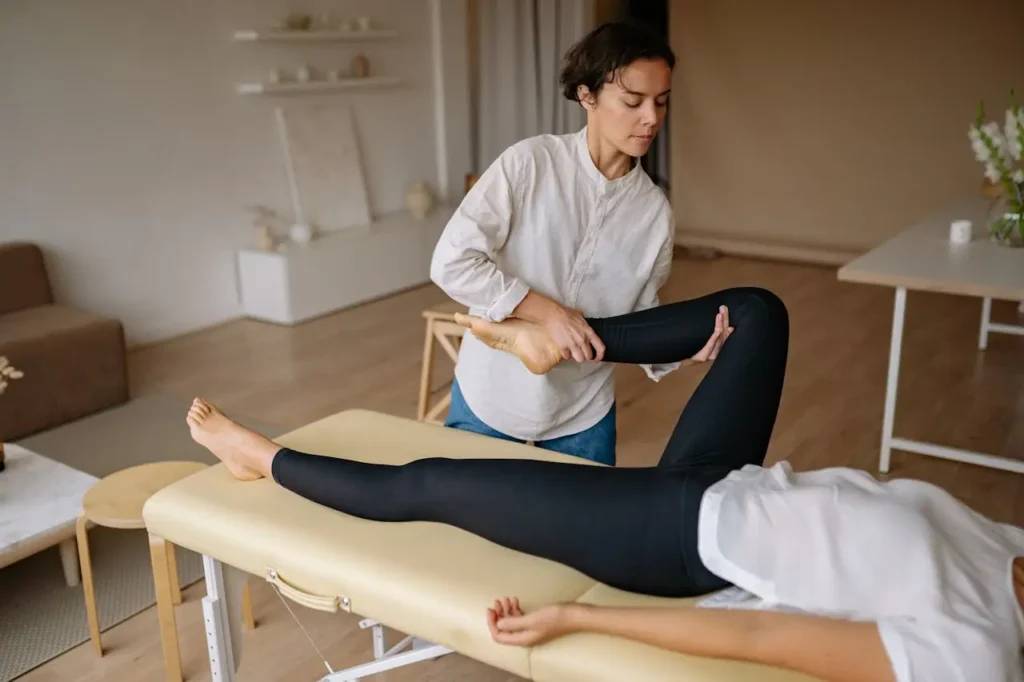 Mujer fisioterapeuta realizando un masaje terapéutico a una pierna de una chica recostada sobre una mesa