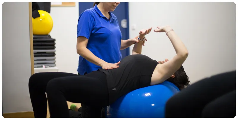 Mujer embaraza en una pelota de pilates recibiendo masajes abdominales